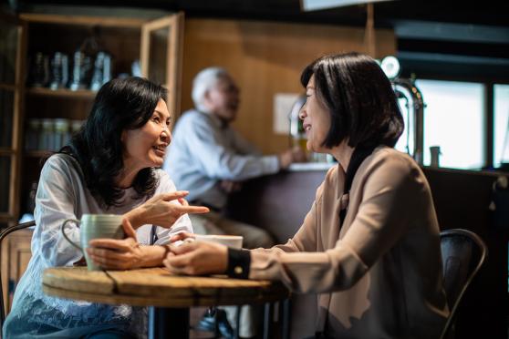 Two women sitting at a table, each holding a coffee mug
